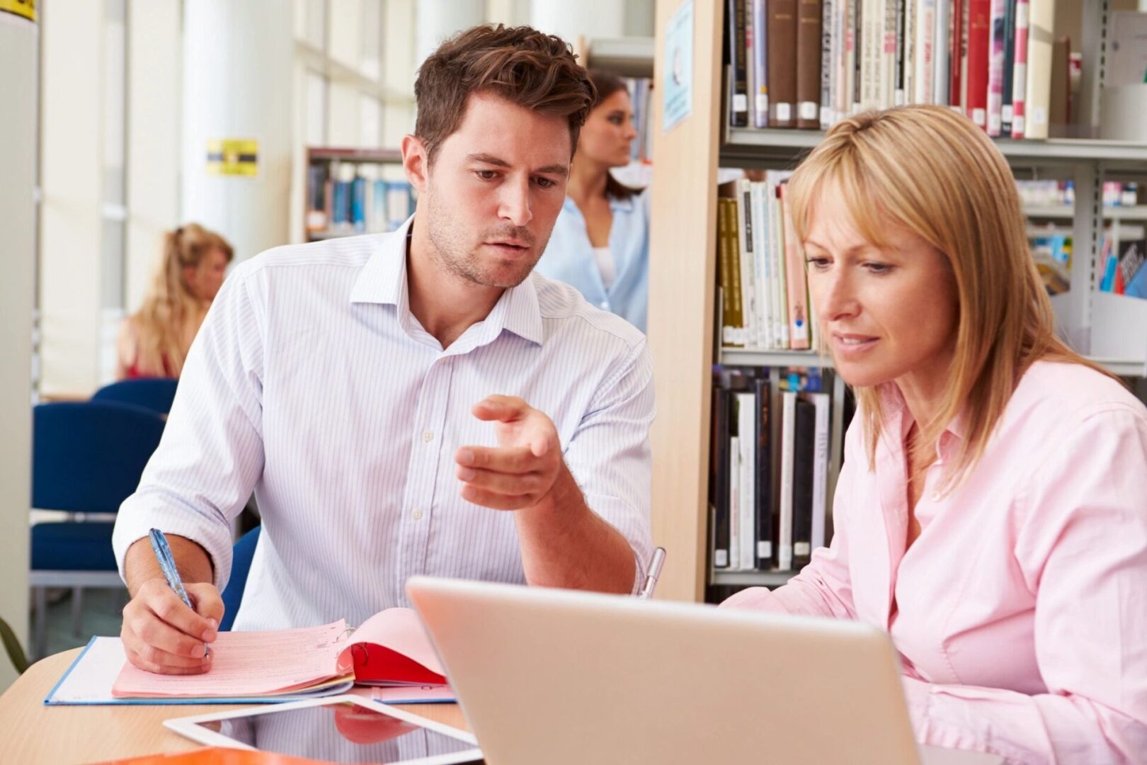 A man and woman sitting at a table looking at a laptop.